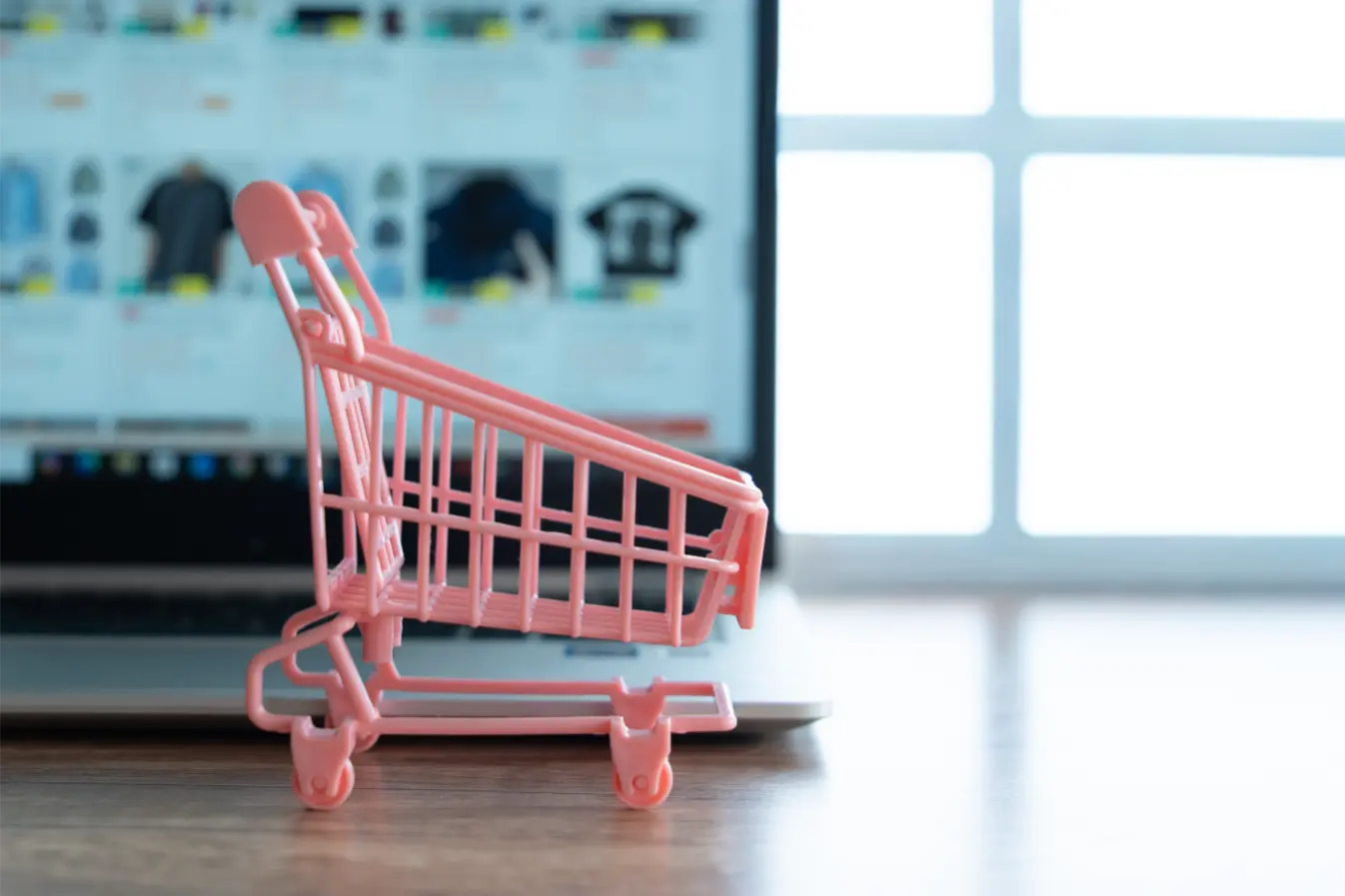 
a-small-pink-shopping-cart-in-front-of-a-laptop